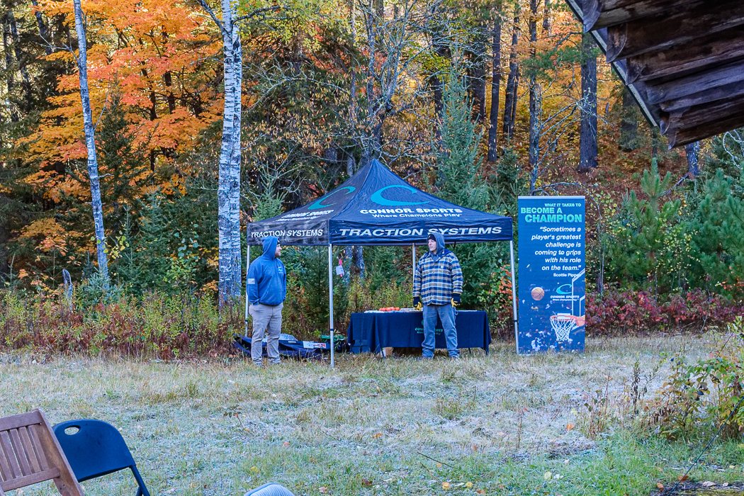 A sponsor’s display tent and banner in a frosty clearing, with orange maples and white birches behind