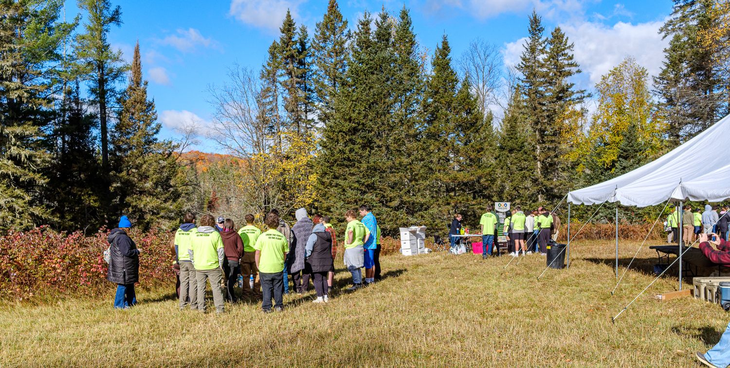 Groups of students in green shirts gathered at two outdoor stations in the meadow