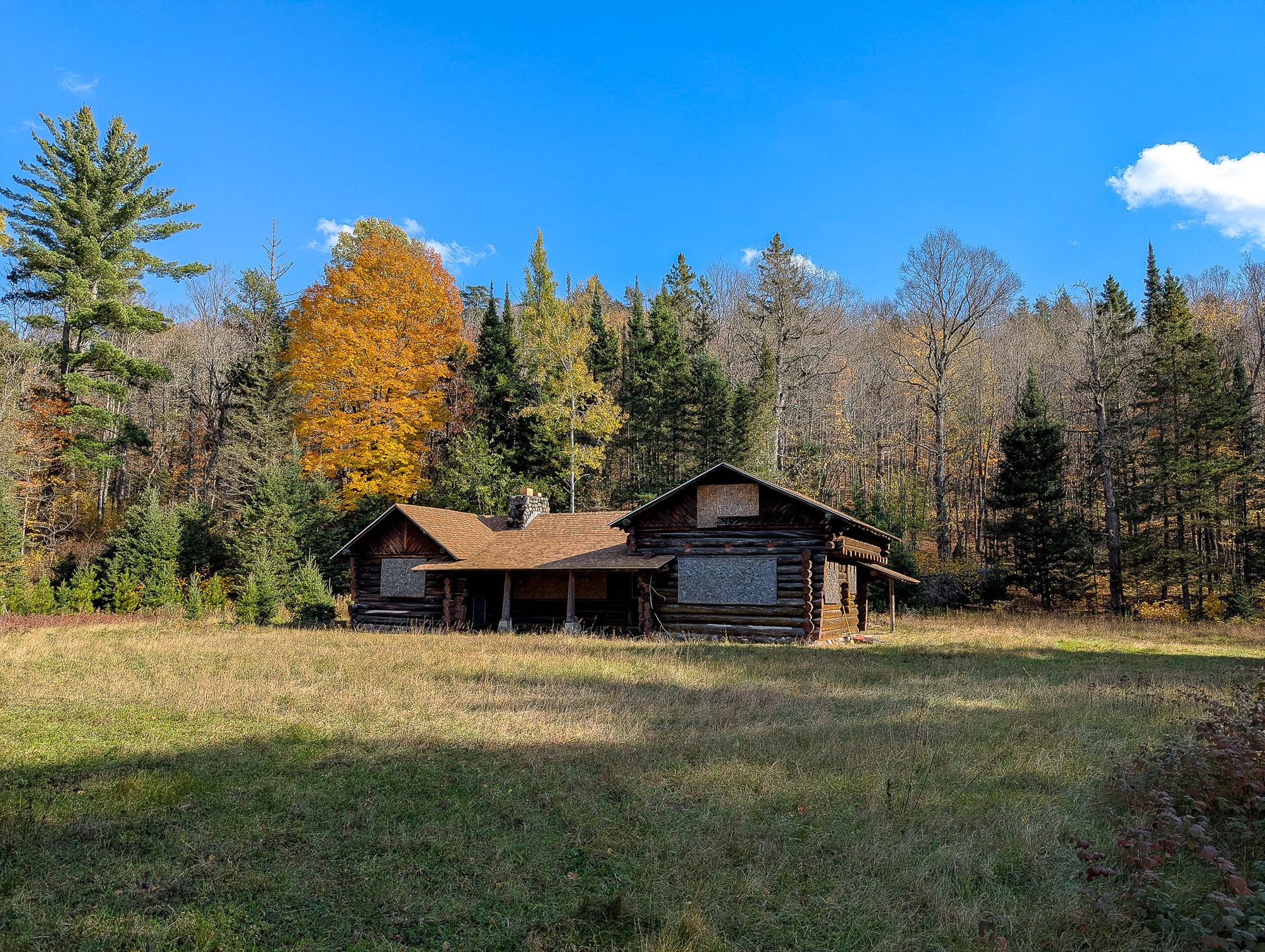 The log cabin at Cooks Run seen across the meadow, with maples in autumn color behind it