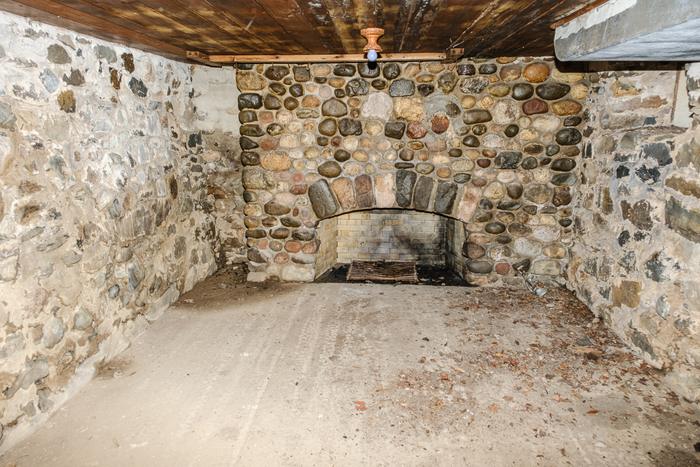 A basement room with a fieldstone wall and a small fireplace