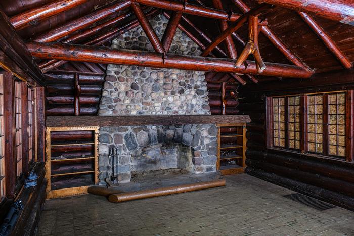 A fieldstone fireplace with built-in shelves under log trusses