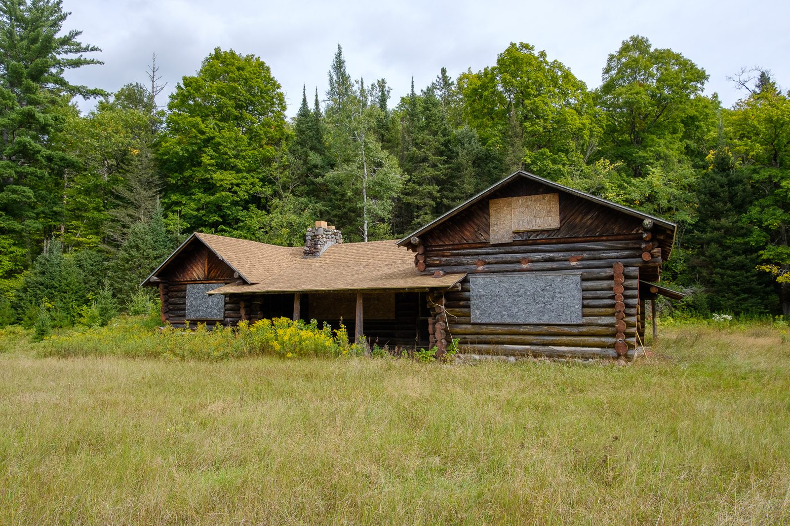 The log cabin seen across the meadow, its windows covered with plywood boards